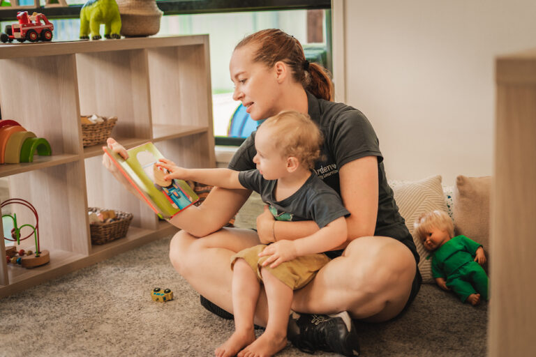 An Arden educator reading a book with a toddler on her lap