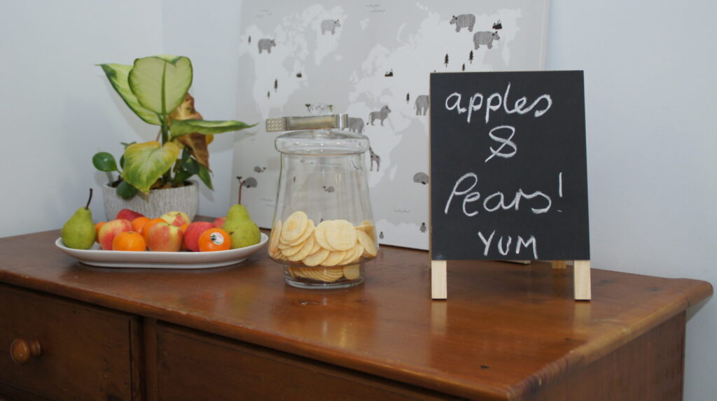 A homely nook with fruit, a glass jar and a chalkboard reading apples and pears yum