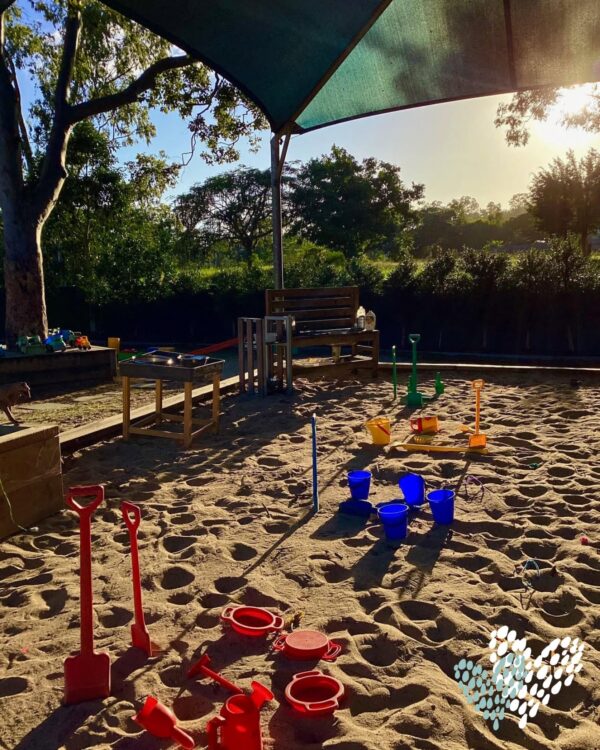 Sunlit outdoor sandpit with buckets and spades under shade sails at Arden Early Learning Airlie Beach